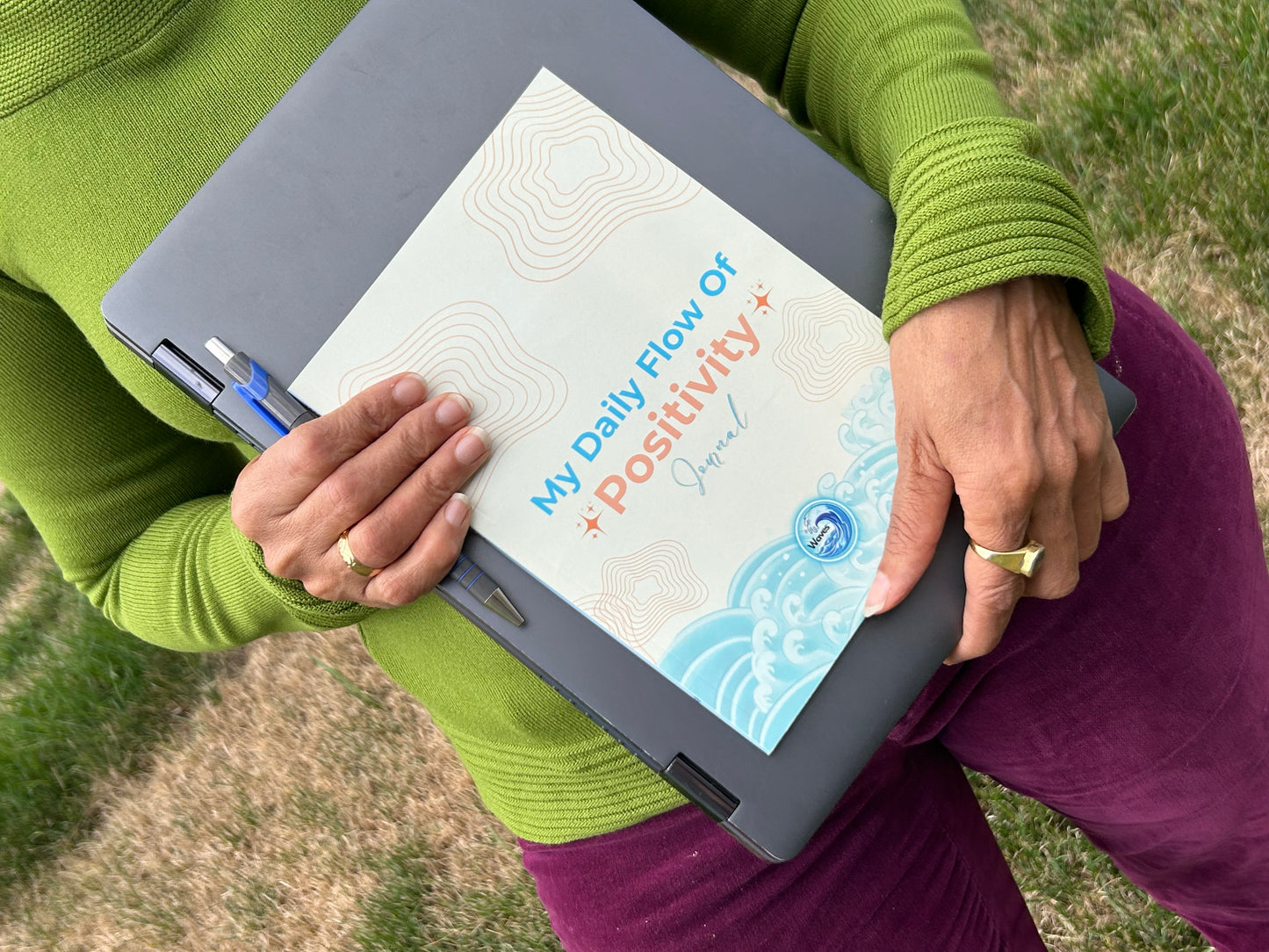 Person holding a laptop with a book titled 'My Daily Flow of Positivity' on the screen.