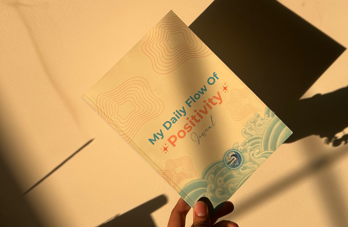 Hand holding a 'My Daily Flow of Positivity' journal with a yellow background
