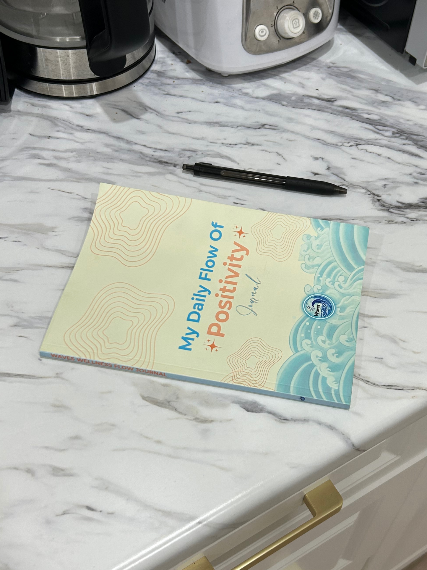 Notebook titled 'My Daily Flow of Positivity' on a marble countertop with a pen next to it.