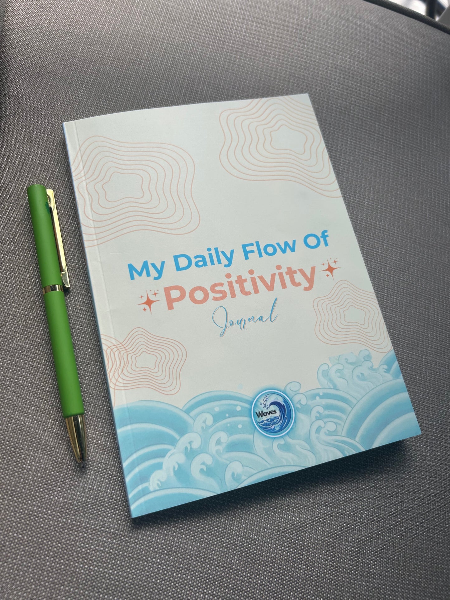 Journal titled 'My Daily Flow Of Positivity' with a green pen on a gray surface