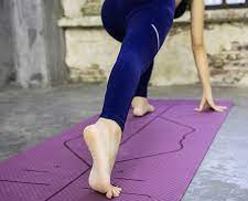 Person in blue leggings standing on a purple yoga mat outdoors.