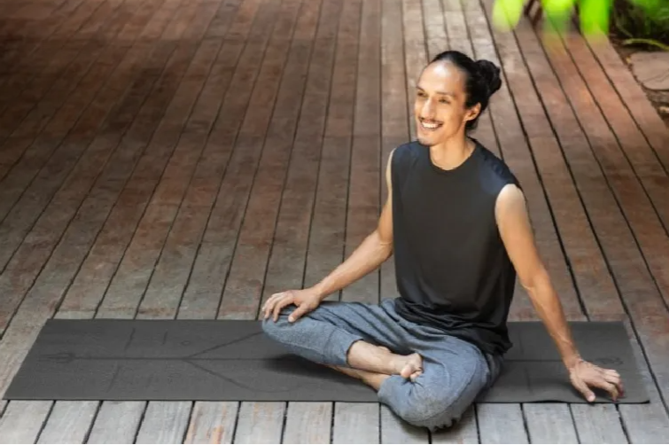 Person sitting on a yoga mat outdoors on a wooden deck